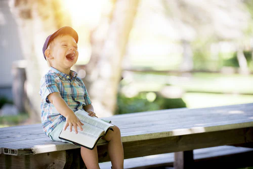 Beginning Readers keeper young boy reading on a picnic table, laughing