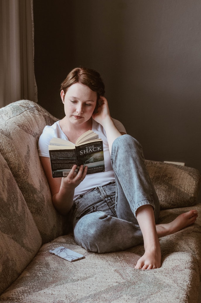 17 Ways to Keep Your Middle Schooler Interested In Reading woman reading book on a couch