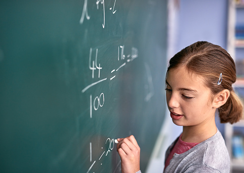 Cropped shot of an elementary school girl writing on a blackboard in class girl writing on a chalk board