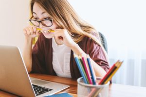 Woman biting a pencil, sitting in front of her laptop.
