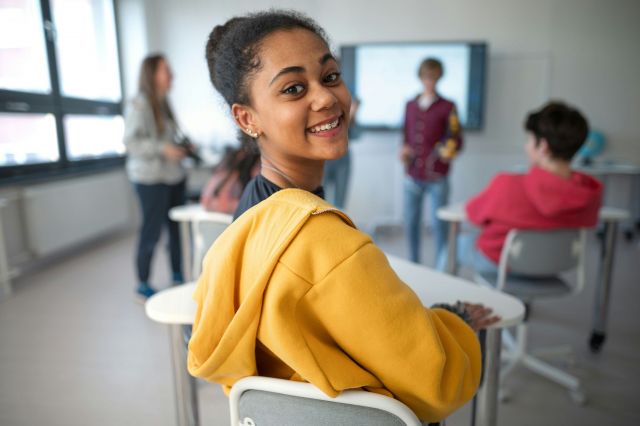 Student posing for a picture, while seated at her desk.