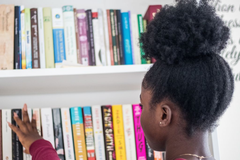 Little girl looking at books on a shelf.