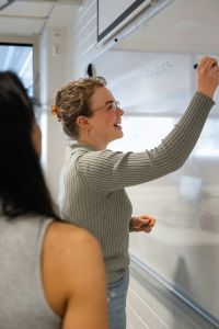 Person writing on a whiteboard in a classroom.