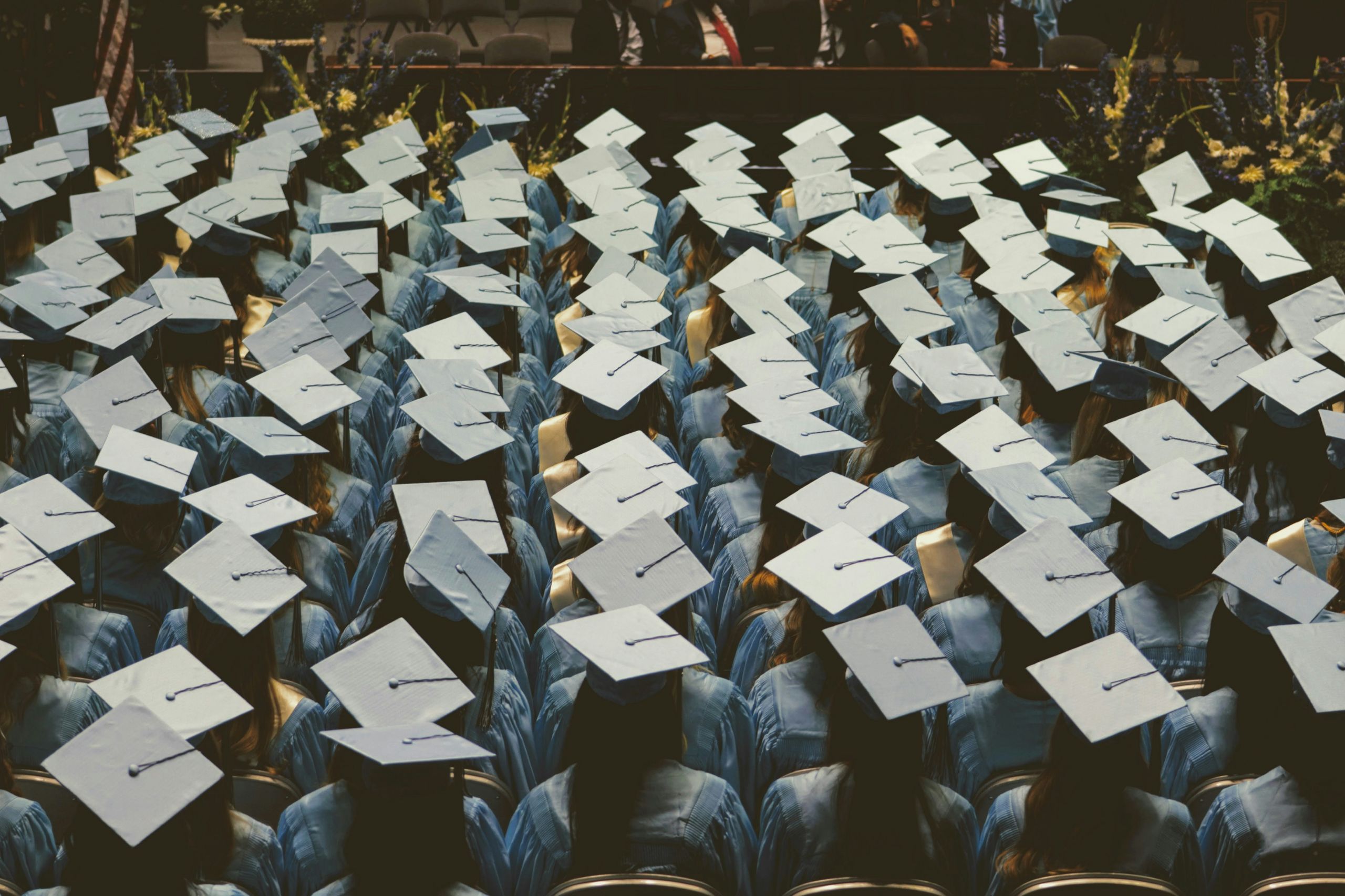 joshua-hoehne-iggWDxHTAUQ-unsplash People in graduation outfits, sitting down and waiting.