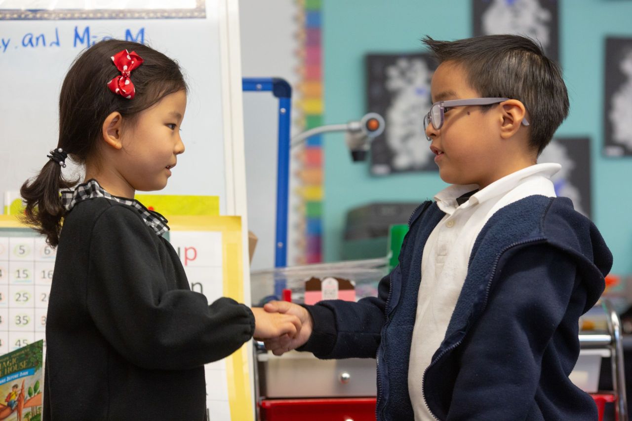 Two students practicing greeting each other with a handshake.